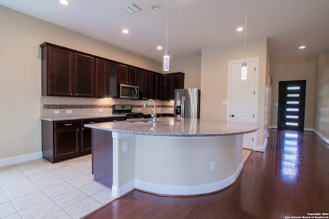 kitchen featuring light stone countertops, light hardwood / wood-style flooring, stainless steel appliances, dark brown cabinetry, and pendant lighting