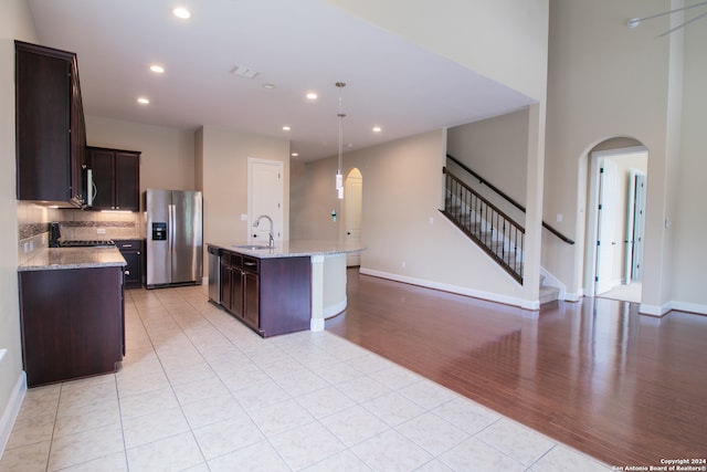 kitchen featuring appliances with stainless steel finishes, a center island with sink, light wood-type flooring, backsplash, and hanging light fixtures