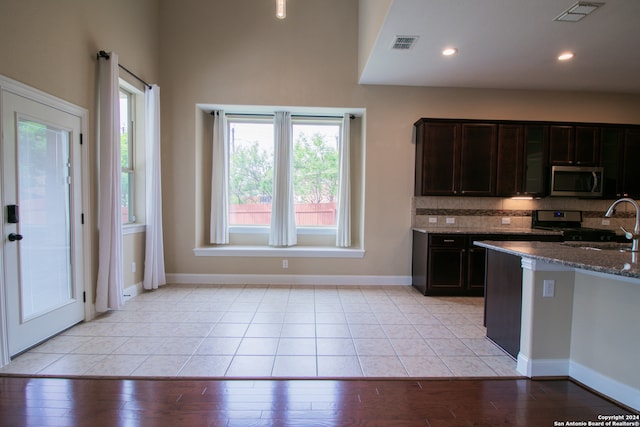 kitchen with dark brown cabinets, dark stone countertops, backsplash, light hardwood / wood-style floors, and stainless steel appliances