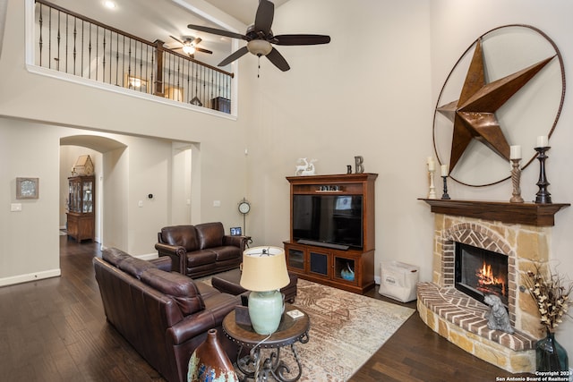 living room with dark hardwood / wood-style flooring, ceiling fan, a towering ceiling, and a stone fireplace