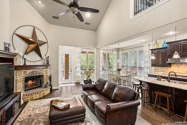 living room with high vaulted ceiling, a stone fireplace, dark hardwood / wood-style floors, ceiling fan, and sink