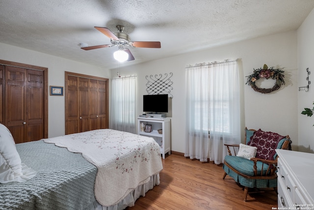 bedroom featuring ceiling fan, two closets, a textured ceiling, and light hardwood / wood-style floors