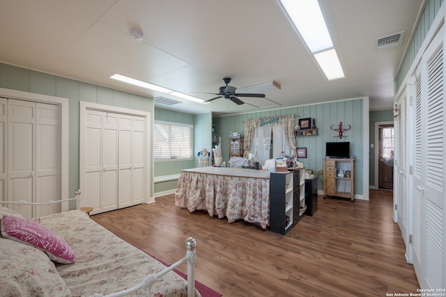 bedroom featuring wood-type flooring, ceiling fan, and two closets