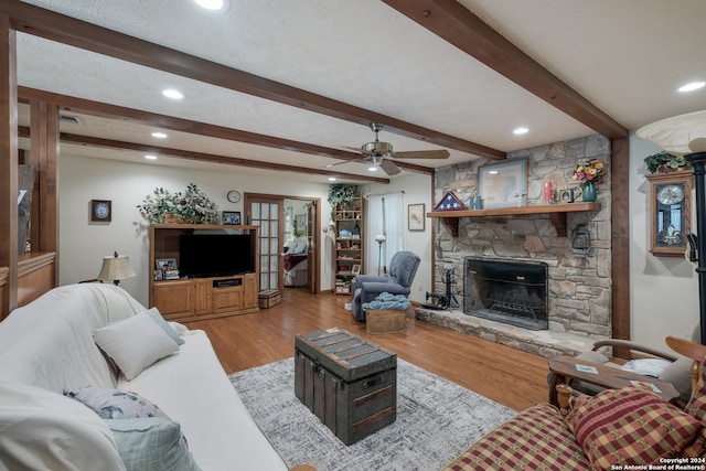 living room featuring ceiling fan, a fireplace, light hardwood / wood-style flooring, a textured ceiling, and beam ceiling