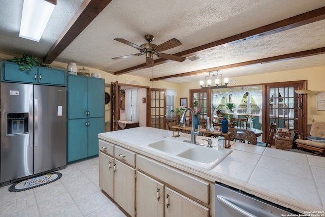 kitchen featuring stainless steel appliances, sink, pendant lighting, beamed ceiling, and ceiling fan with notable chandelier