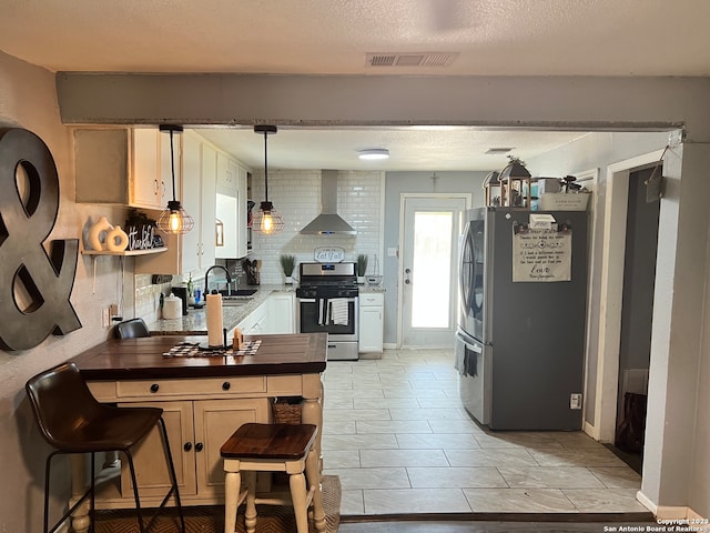 kitchen featuring backsplash, appliances with stainless steel finishes, a textured ceiling, wall chimney exhaust hood, and decorative light fixtures