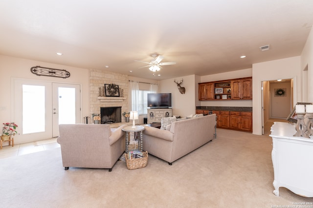 carpeted living room with ceiling fan and a stone fireplace