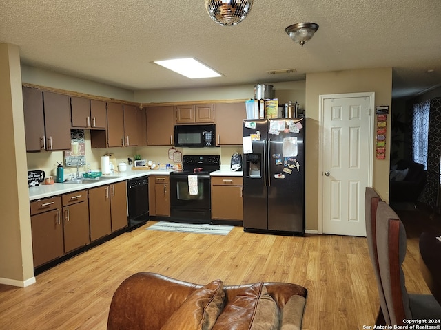 kitchen featuring a textured ceiling, sink, light hardwood / wood-style floors, and black appliances