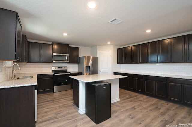 kitchen with stainless steel appliances, sink, a kitchen island, hardwood / wood-style floors, and tasteful backsplash