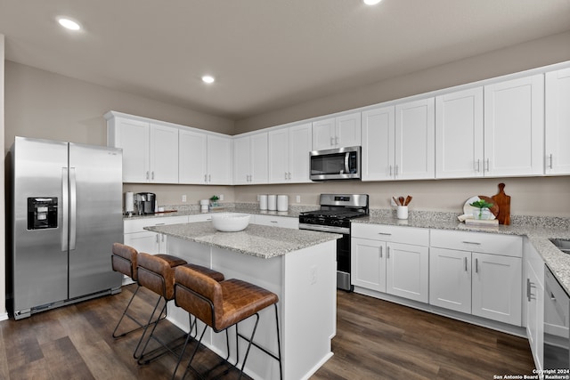 kitchen with appliances with stainless steel finishes, a center island, light stone countertops, dark hardwood / wood-style floors, and white cabinets