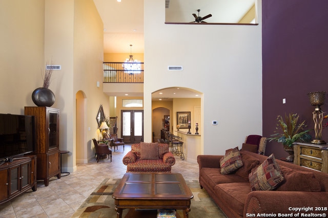 tiled living room featuring ceiling fan with notable chandelier and a high ceiling