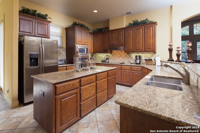 kitchen featuring a wealth of natural light, appliances with stainless steel finishes, a kitchen island, light stone counters, and tasteful backsplash