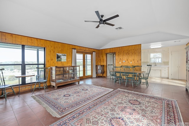 living room with wood walls, dark tile patterned floors, sink, ceiling fan, and lofted ceiling