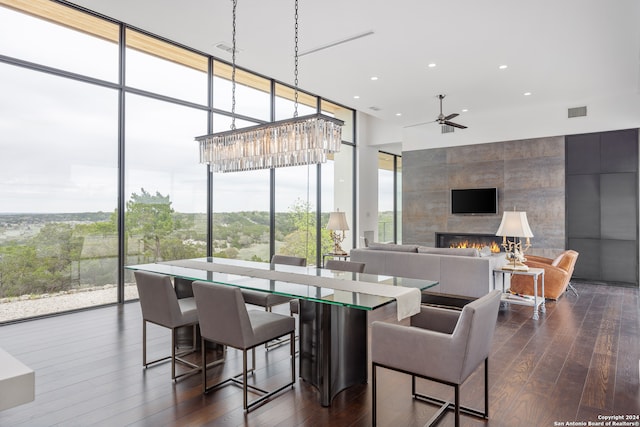 dining room featuring a healthy amount of sunlight, ceiling fan with notable chandelier, a tile fireplace, and dark wood-type flooring