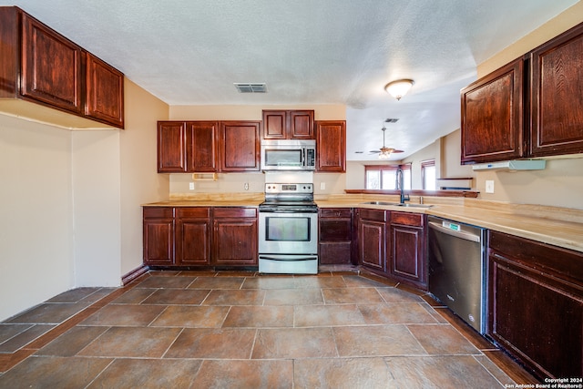 kitchen featuring dark tile floors, stainless steel appliances, sink, ceiling fan, and a textured ceiling