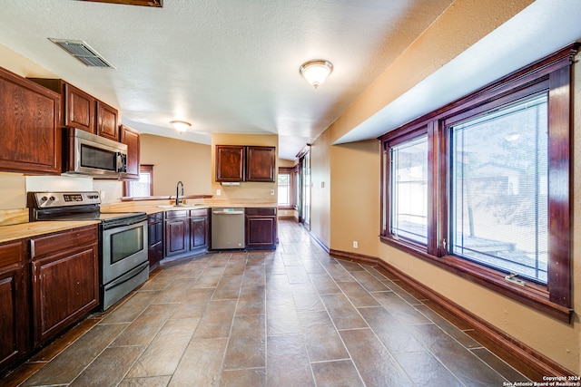 kitchen with a textured ceiling, dark tile flooring, stainless steel appliances, and sink