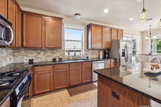 kitchen featuring appliances with stainless steel finishes, light tile floors, sink, dark stone counters, and decorative light fixtures