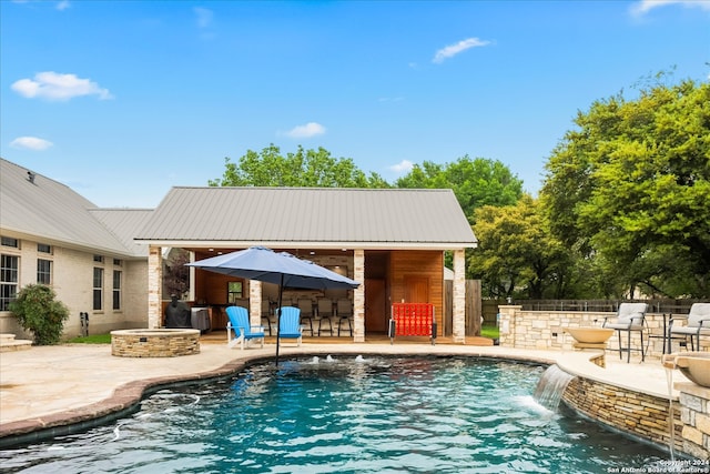 view of pool featuring pool water feature, a bar, an outdoor fire pit, and a patio