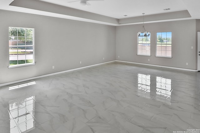 empty room with a healthy amount of sunlight, light tile floors, and a tray ceiling