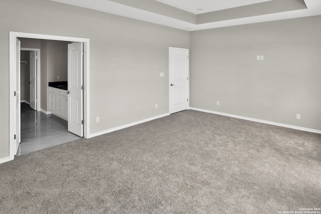 empty room with a raised ceiling and dark colored carpet