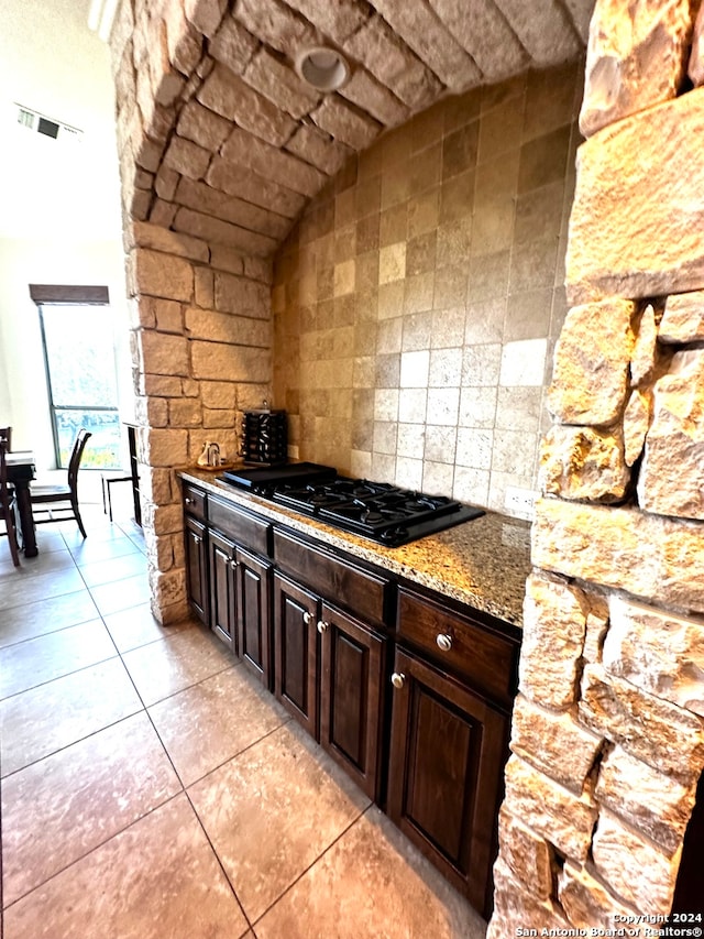 interior space with tasteful backsplash, light tile patterned floors, light stone counters, black gas stovetop, and dark brown cabinetry