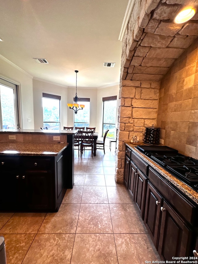 kitchen featuring hanging light fixtures, light tile patterned floors, dark stone countertops, dark brown cabinets, and ornamental molding