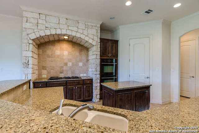 kitchen featuring black double oven, sink, light stone countertops, and dark brown cabinets