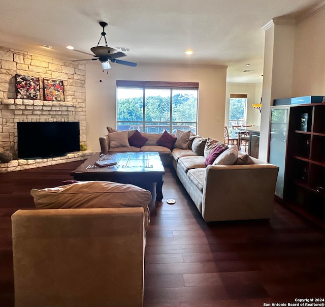 living room with a textured ceiling, dark hardwood / wood-style floors, a stone fireplace, ornamental molding, and ceiling fan