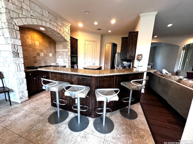 kitchen featuring light stone countertops, light hardwood / wood-style flooring, a kitchen bar, kitchen peninsula, and black oven