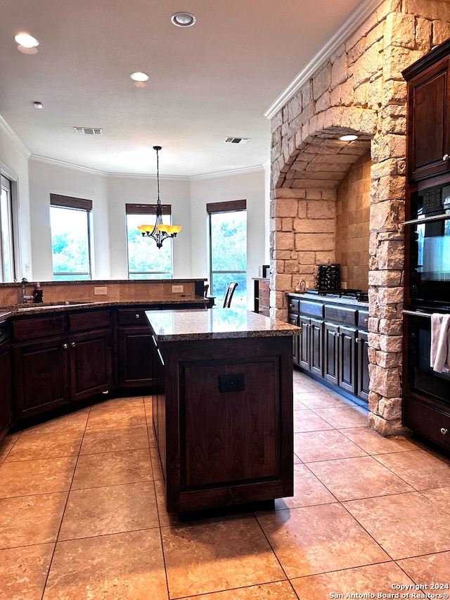 kitchen with crown molding, light stone counters, a healthy amount of sunlight, and a kitchen island