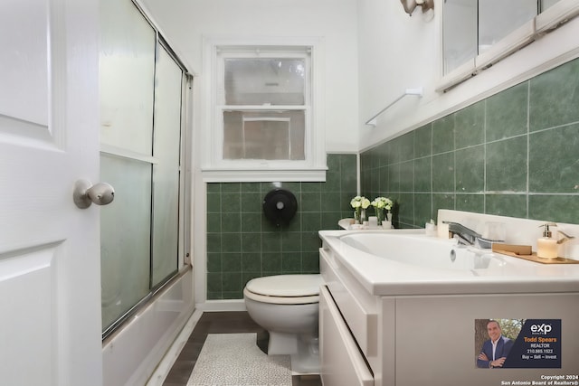 full bathroom featuring tile walls, hardwood / wood-style floors, bath / shower combo with glass door, oversized vanity, and toilet