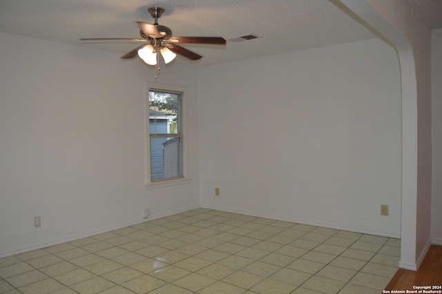 spare room featuring ceiling fan, light tile flooring, and a textured ceiling