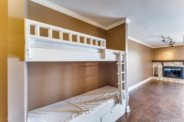 unfurnished bedroom featuring ornamental molding, dark hardwood / wood-style flooring, a stone fireplace, and rail lighting