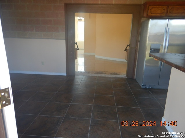 kitchen featuring stainless steel fridge with ice dispenser, dark tile flooring, and tile counters