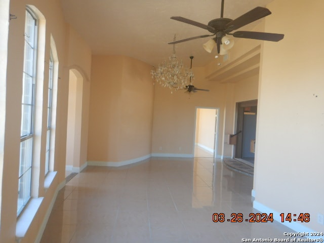 tiled spare room featuring ceiling fan with notable chandelier