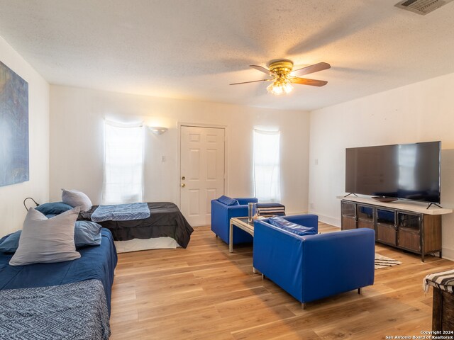 living room featuring light hardwood / wood-style flooring, ceiling fan, and a textured ceiling