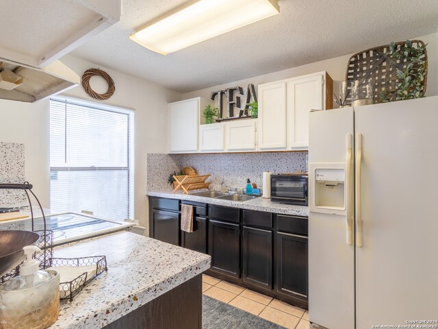 kitchen with white fridge with ice dispenser, a textured ceiling, sink, light tile flooring, and white cabinetry