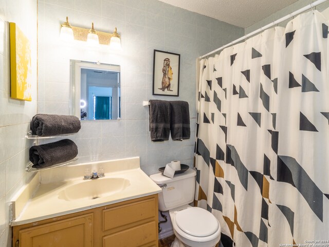 bathroom with tile walls, toilet, vanity with extensive cabinet space, and a textured ceiling