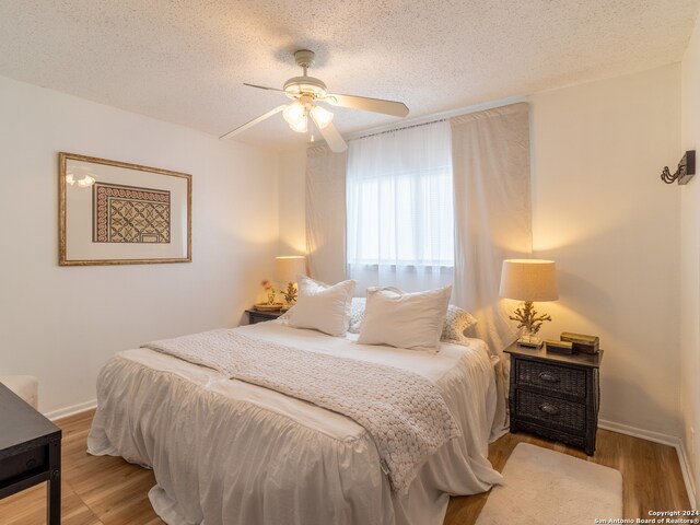 bedroom featuring light hardwood / wood-style floors, ceiling fan, and a textured ceiling