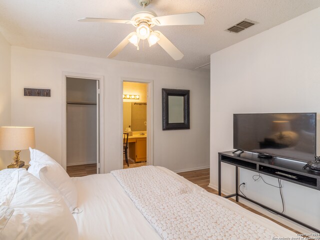 bedroom featuring connected bathroom, light hardwood / wood-style floors, ceiling fan, and a textured ceiling