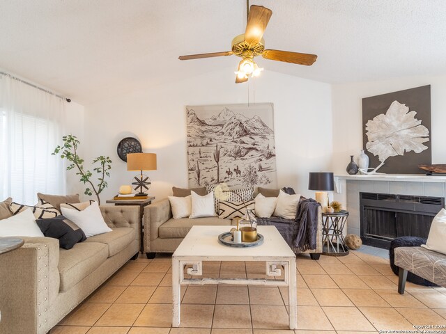 tiled living room with vaulted ceiling, ceiling fan, and a tile fireplace