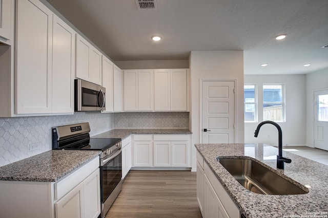 kitchen with sink, white cabinetry, stainless steel appliances, light stone counters, and light hardwood / wood-style floors