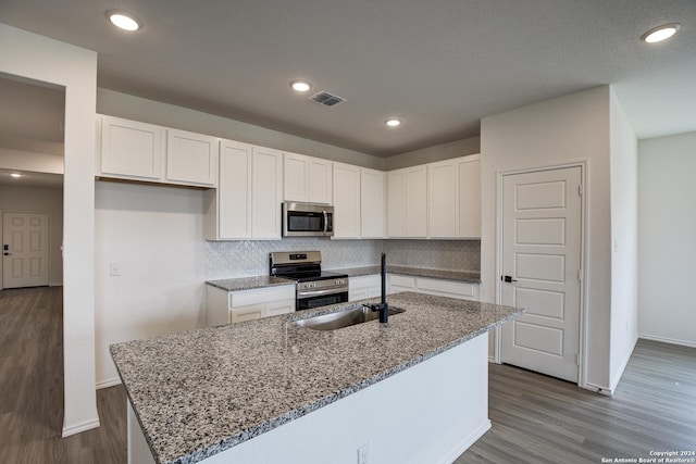 kitchen with white cabinetry, wood-type flooring, appliances with stainless steel finishes, stone counters, and a kitchen island with sink