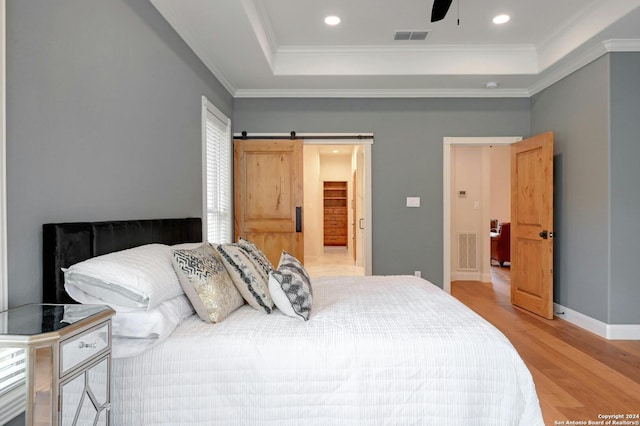 bedroom featuring ceiling fan, a barn door, light hardwood / wood-style floors, and a raised ceiling