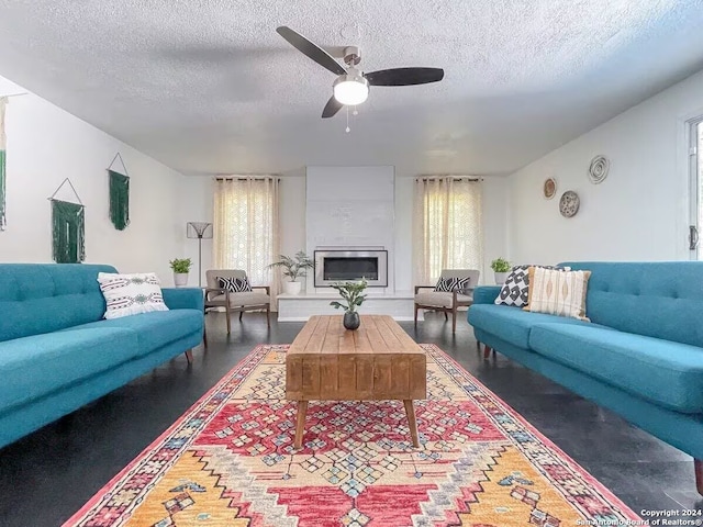 living room with a textured ceiling, a wealth of natural light, ceiling fan, and a large fireplace