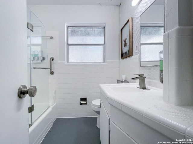 full bathroom with tile walls, vanity, toilet, and shower / bath combination with glass door