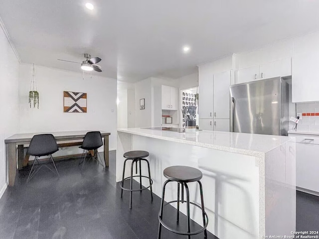 kitchen featuring stainless steel refrigerator, white cabinetry, light stone counters, tasteful backsplash, and ceiling fan