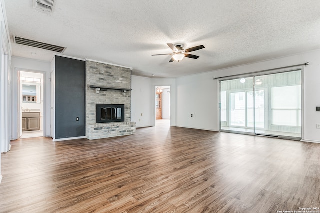 unfurnished living room featuring a brick fireplace, ceiling fan, crown molding, a textured ceiling, and hardwood / wood-style floors