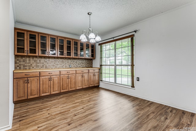 interior space featuring decorative light fixtures, backsplash, a notable chandelier, light hardwood / wood-style floors, and a textured ceiling