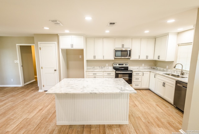 kitchen with appliances with stainless steel finishes, a center island, sink, and light stone counters